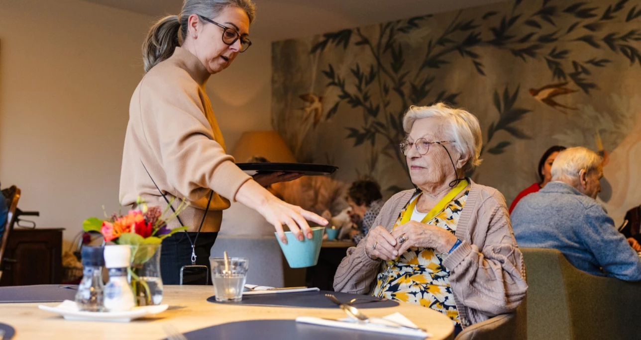 Medewerker schenkt koffie in voor een bewoonster van Valckenborgh